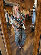 Lu taking a mirror selfie in Leavenworth, KS boutique wearing a floral top and leopard print barrel pants wearing turquoise jewelry. 