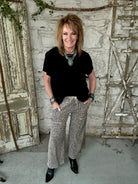 Lu wearing black flowy top and patterned leopard print pants with handmade jewelry in a rustic boutique springfield, mo