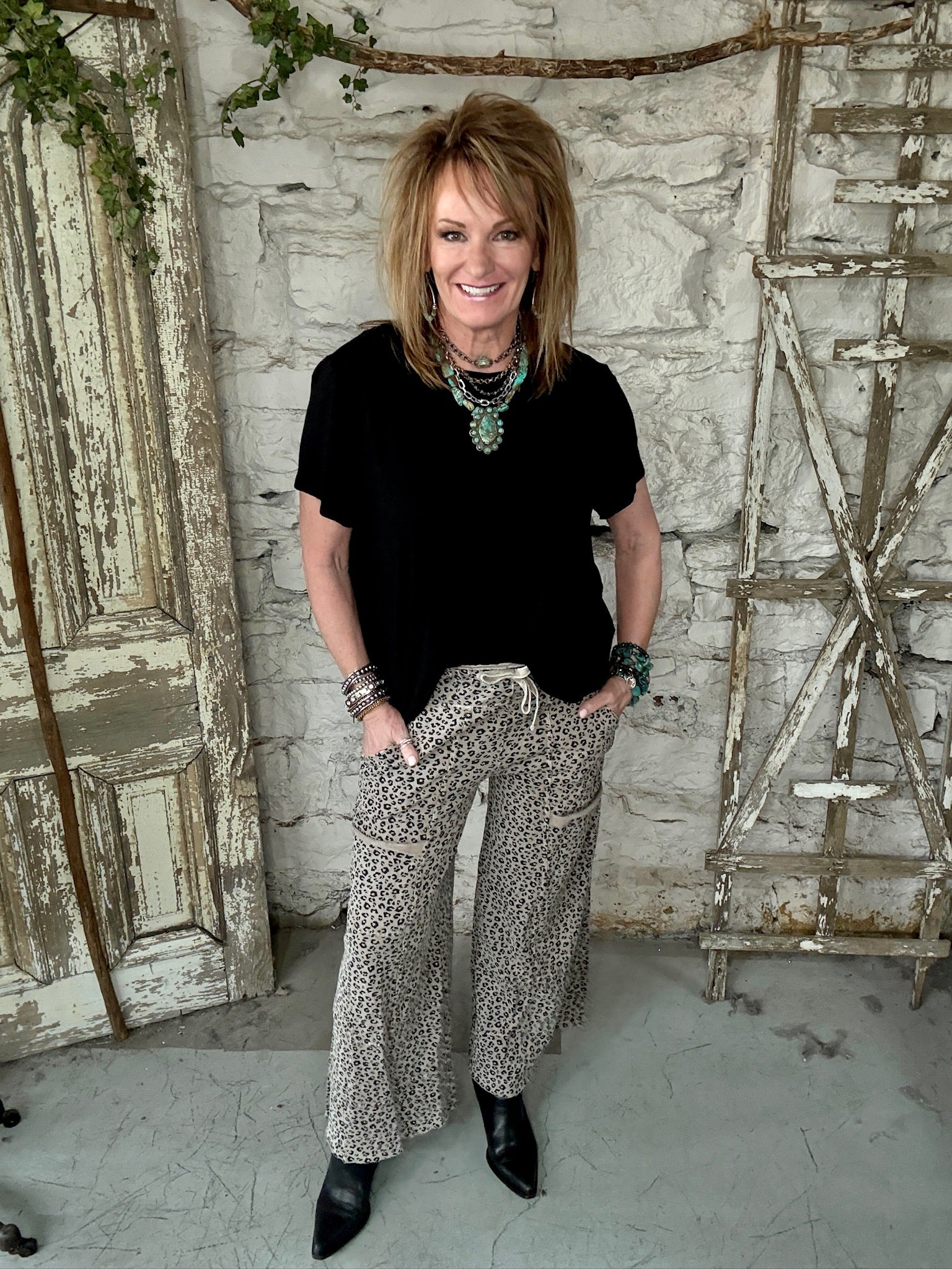 Lu wearing black flowy top and patterned leopard print pants with handmade jewelry in a rustic boutique springfield, mo