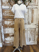 Mannequin wearing a white shirt and beige pants against a rustic wooden door background