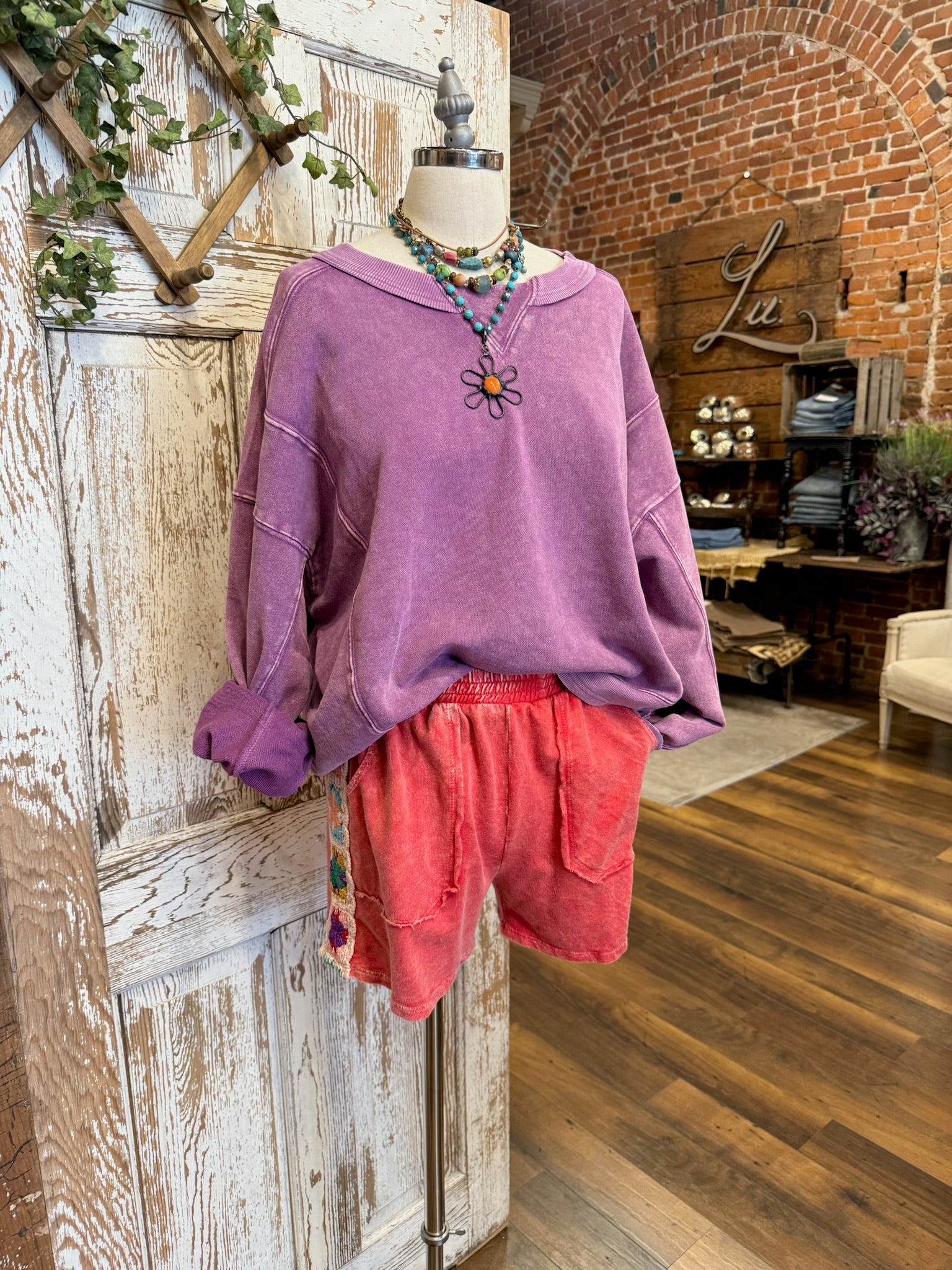 Purple sweatshirt and pink shorts on a mannequin against a rustic brick wall.