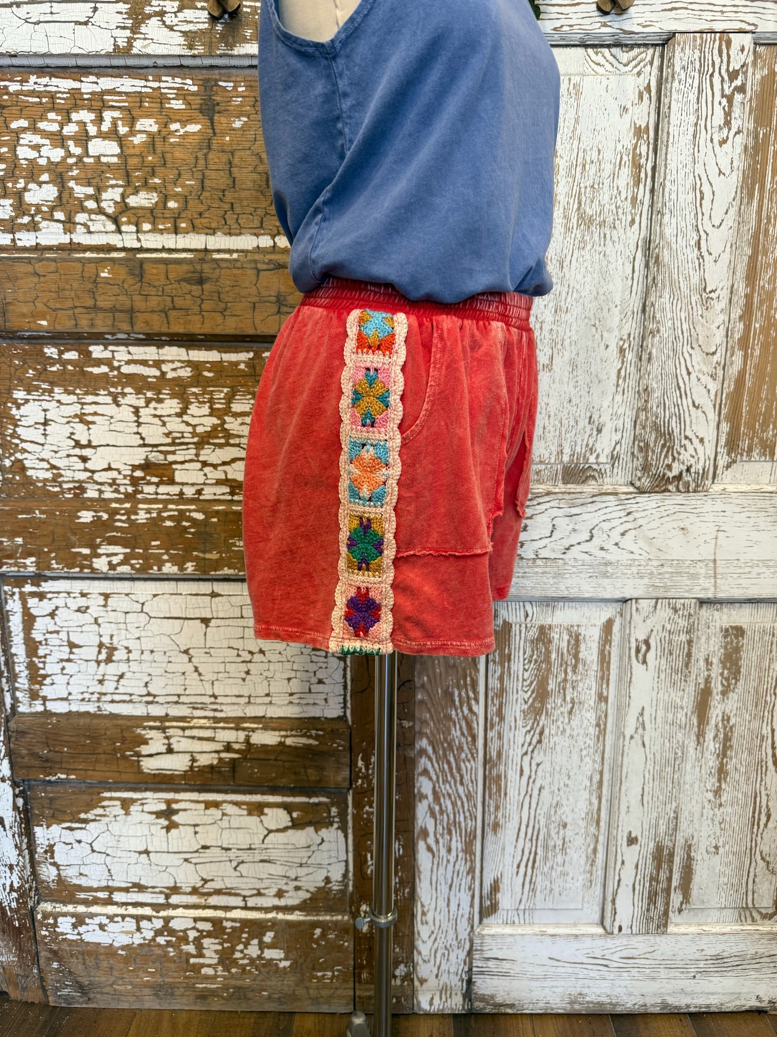 Red shorts with colorful trim worn by a person against a wooden background