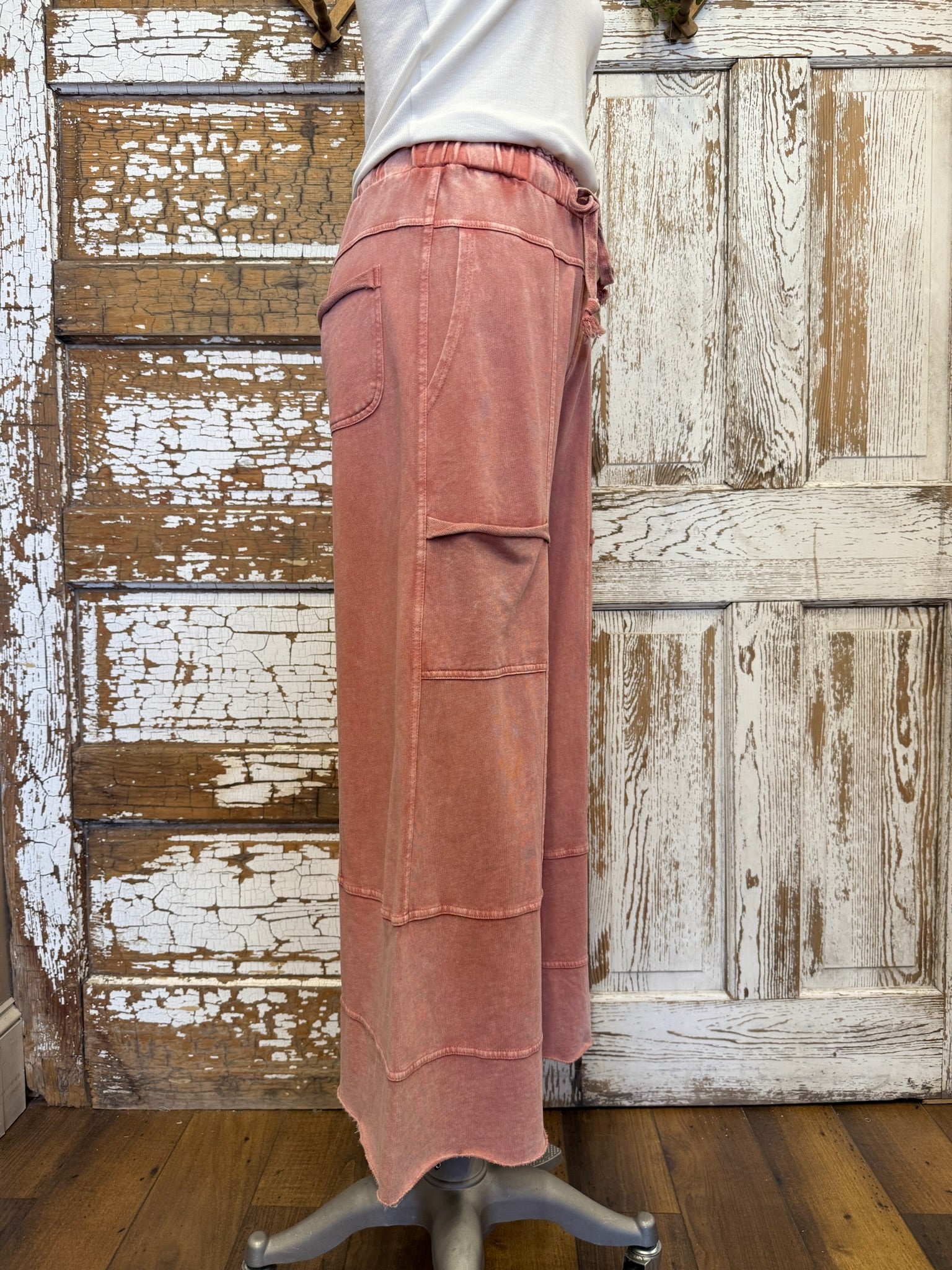 Person wearing pink cargo pants standing in front of a rustic wooden door.