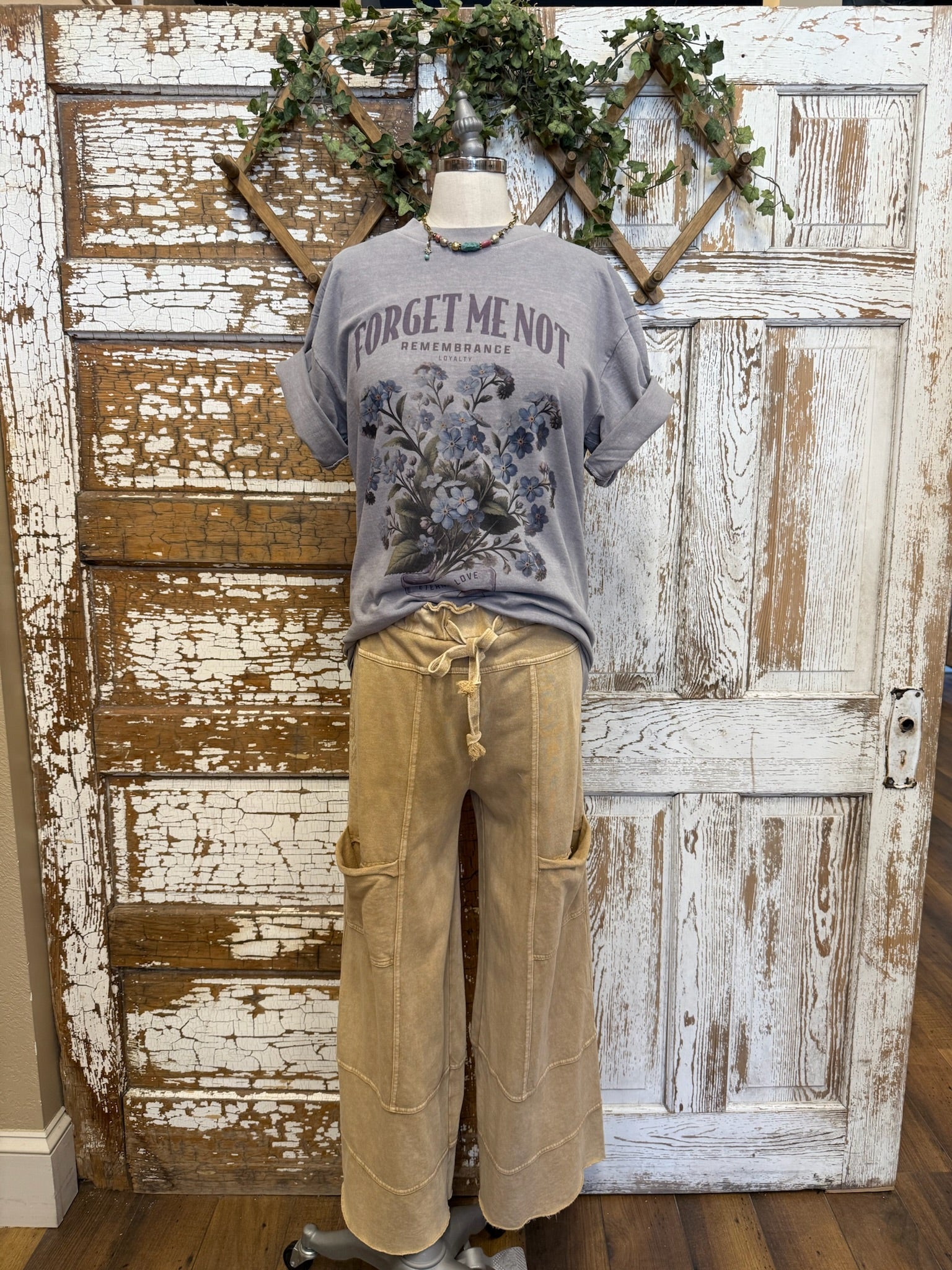Mannequin wearing a gray t-shirt with 'Forget me not' text and beige loungewear pants against a rustic wooden door in Kansas boutique
