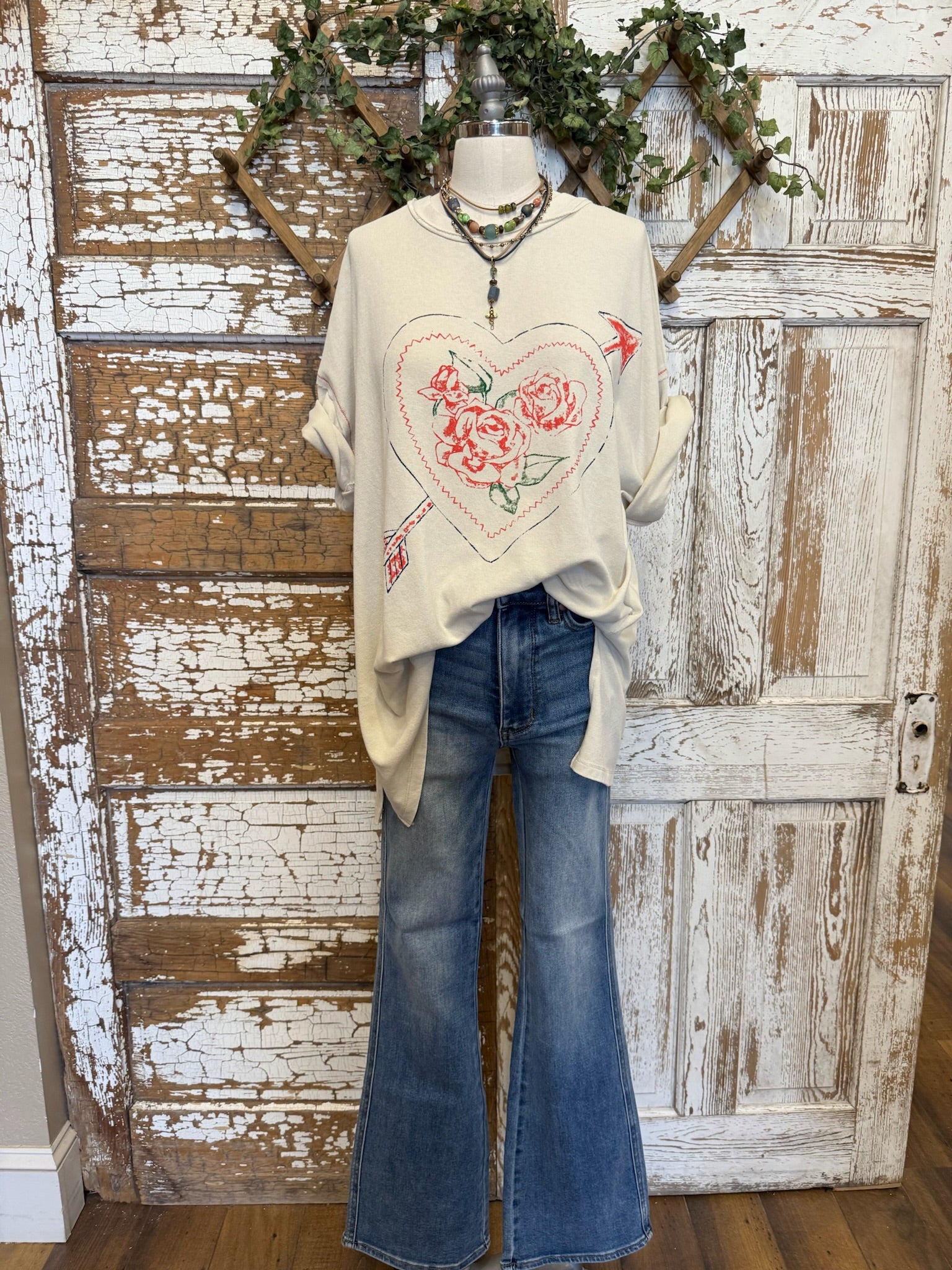 Mannequin wearing a cream graphic tee with floral heart design and jeans with handmade necklaces in Springfield, MO boutique