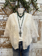 Mannequin wearing a lace cardigan, white shirt, and jeans with handmade turquoise necklaces and cross against a rustic wooden background.