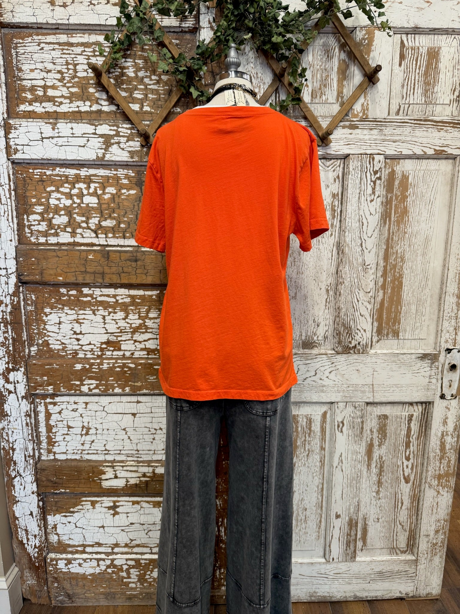 Person wearing an graphic tee shirt and dark pants standing in front of a rustic wooden door.
