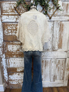 Mannequin wearing a beige lace top and blue jeans against a rustic wooden wall.
