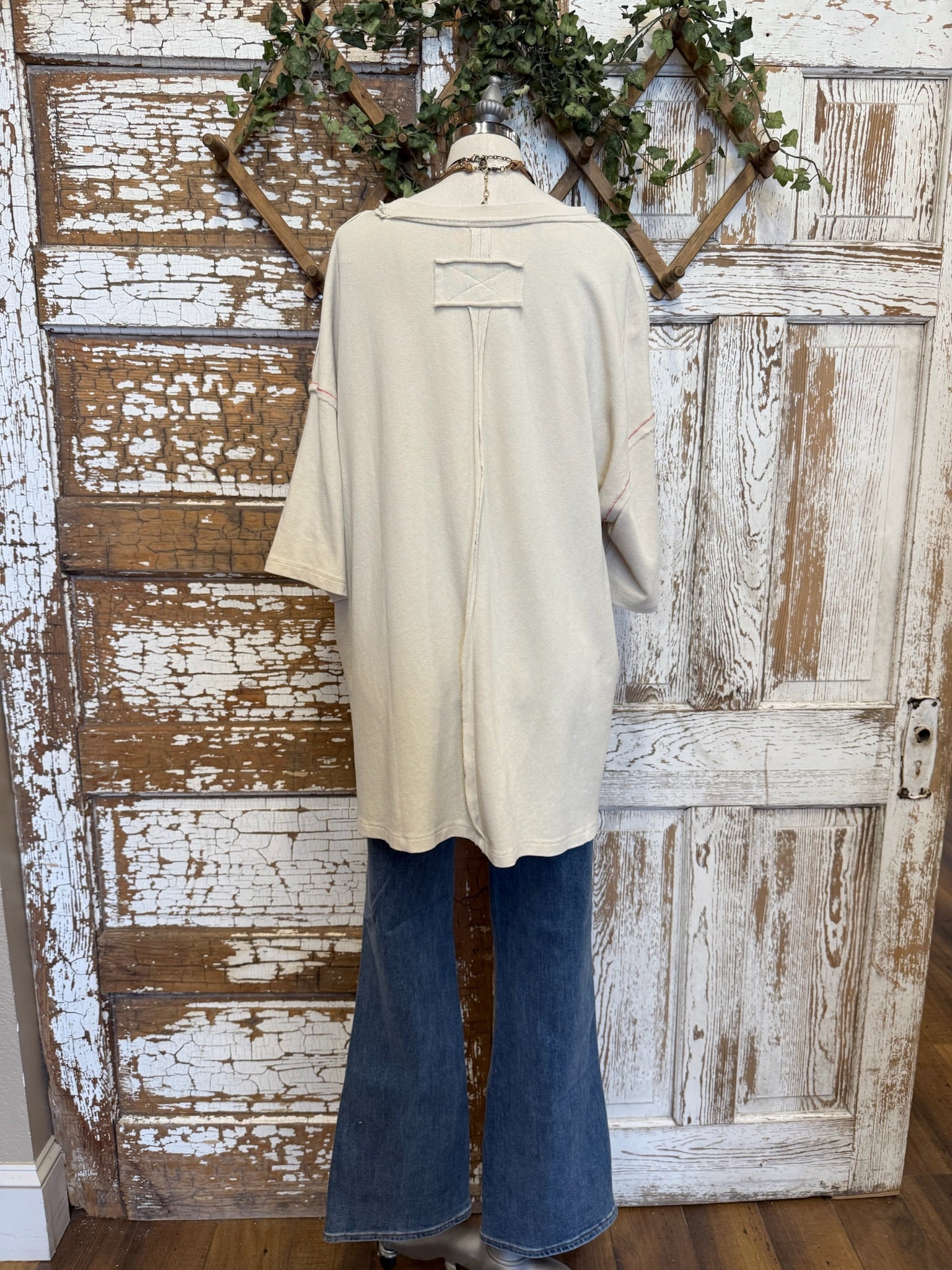 Mannequin wearing a beige top and blue jeans against a rustic wooden door background