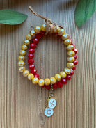Stack of two faceted crystal stretch bracelets in golden yellow and red with gold K and C initial charms and leather tie