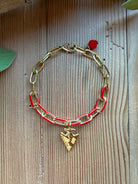 Red and gold enamel paperclip chain bracelet with gold arrowhead charm and red crystal drop on a wood background
