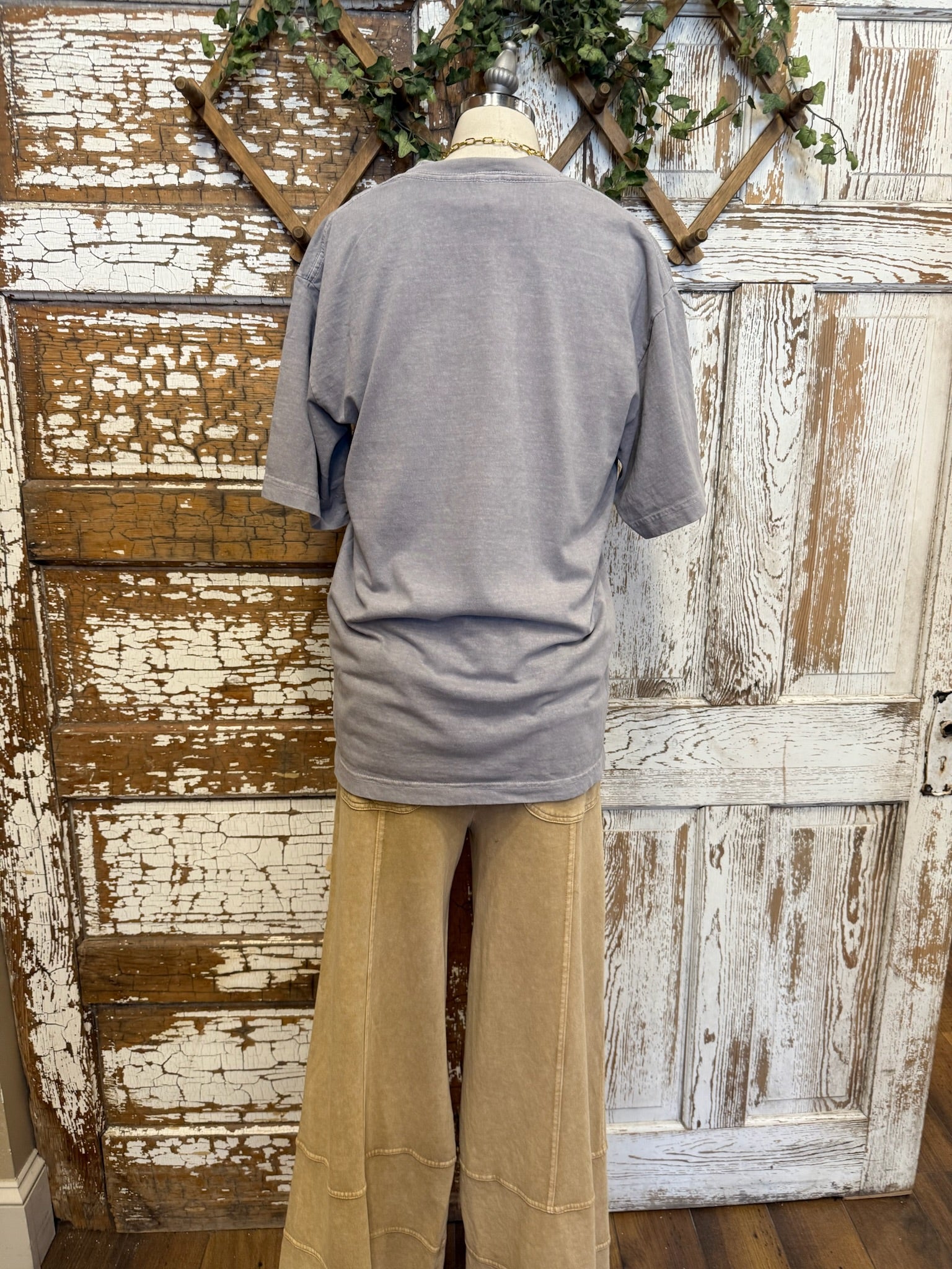 Mannequin wearing a gray t-shirt with 'Forget me not' text and beige loungewear pants against a rustic wooden door in Kansas boutique