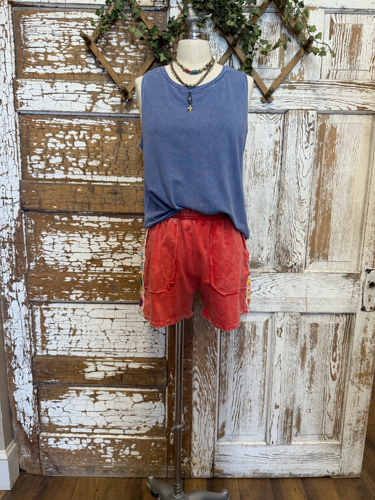 Mannequin wearing a blue sleeveless top and red shorts against a rustic wooden background