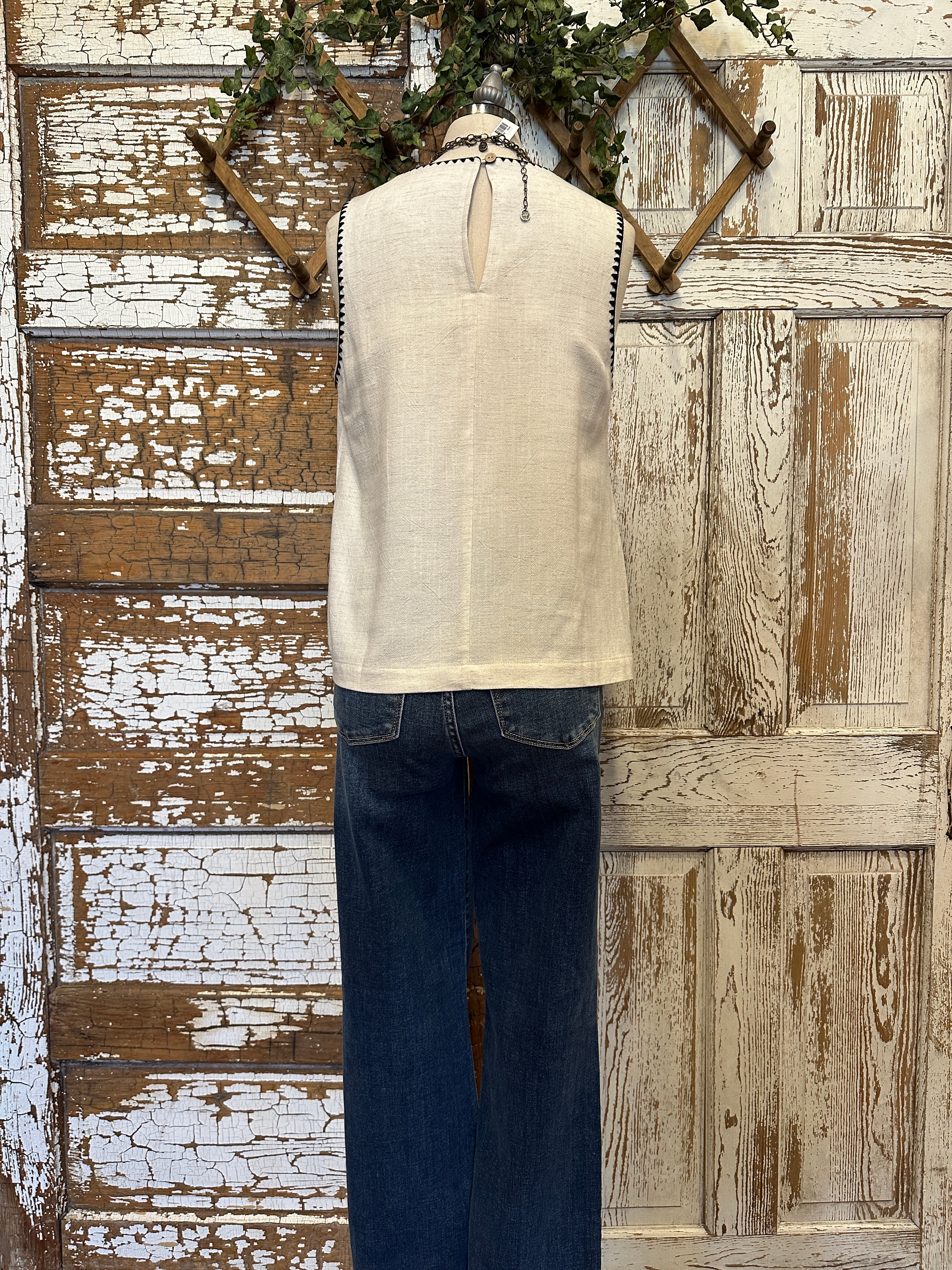 Mannequin wearing a white tank with stitching details and layered handmade necklaces in Leavenworth, KS boutique setting