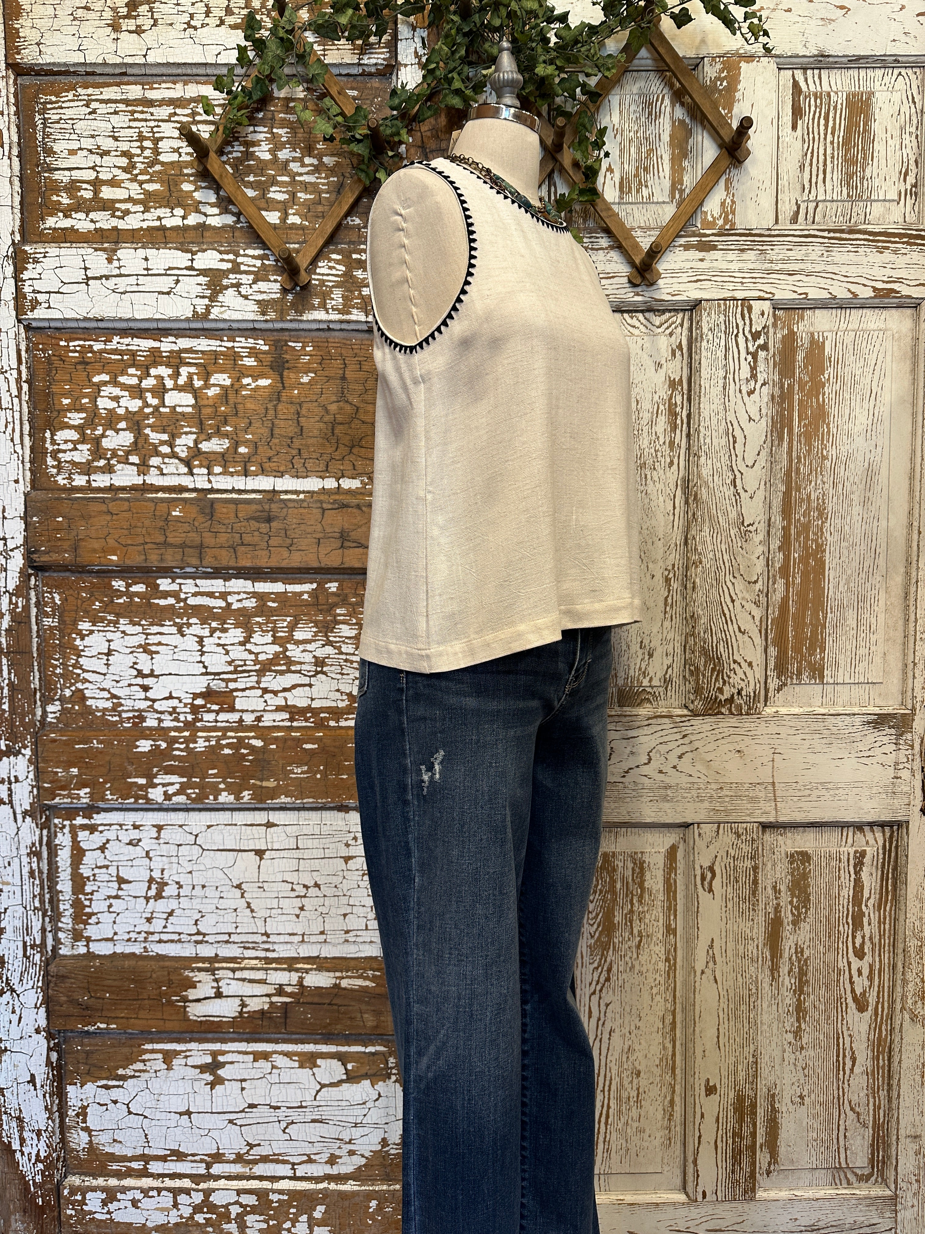 Mannequin wearing a white tank with stitching details and layered handmade necklaces in Leavenworth, KS boutique setting