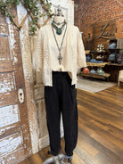 Mannequin wearing a beige lace top and black pants with handmade turquoise jewelry and cross in a boutique setting
