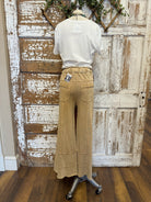 Mannequin wearing a white blouse and tan pants in front of a rustic wooden door.