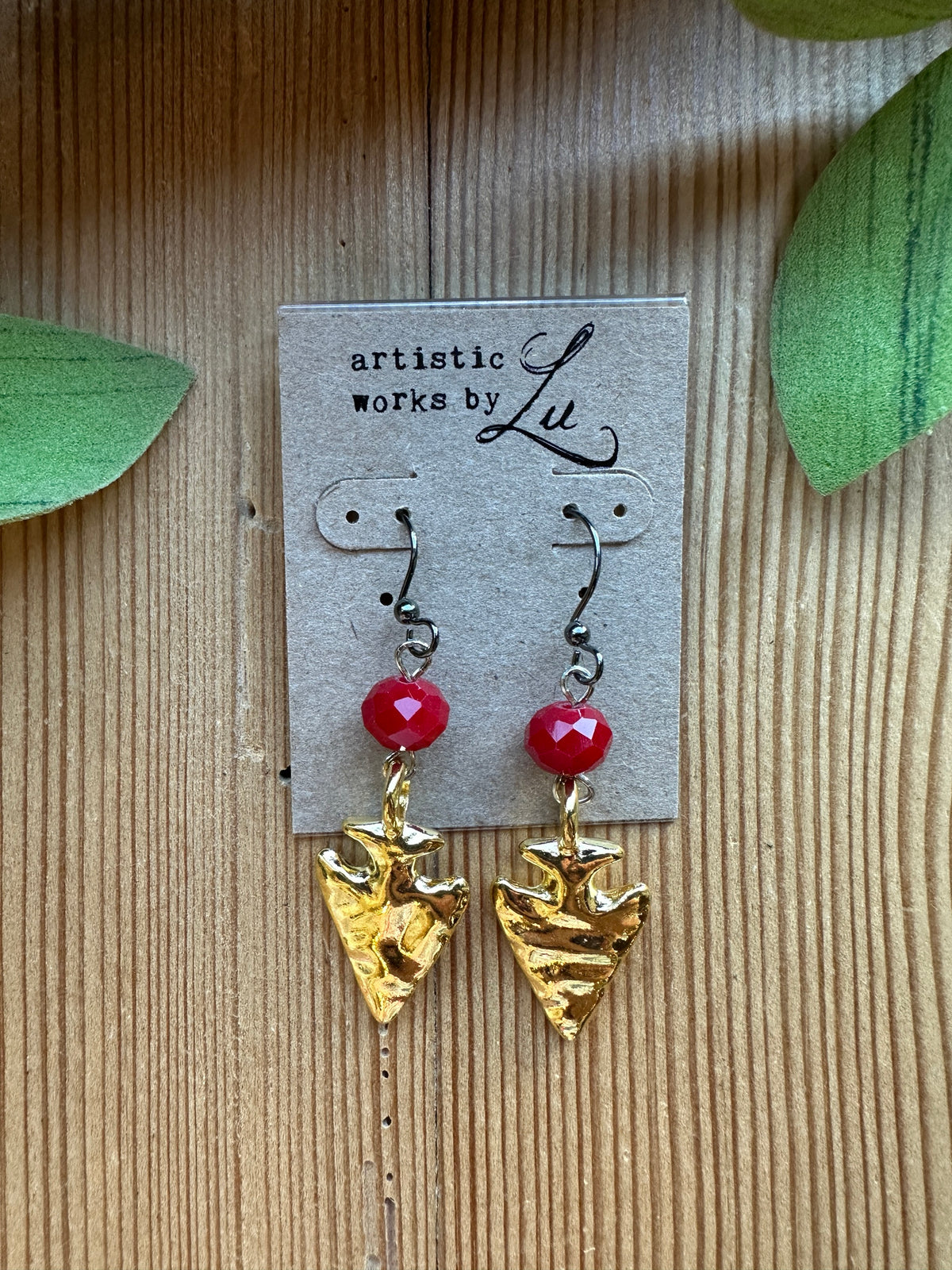 Gold arrowhead dangle earrings with faceted red crystal beads on an Artistic Works By Lu earring card