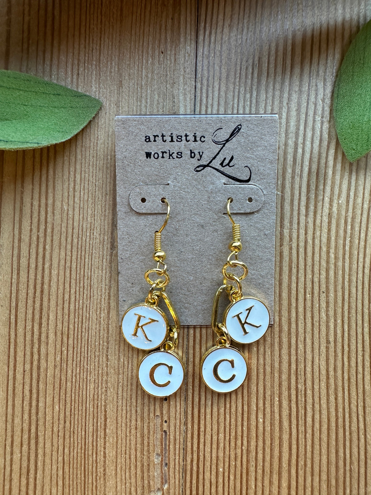 Gold-tone dangle earrings with white enamel K and C initial charms and paperclip link on an Artistic Works By Lu earring card