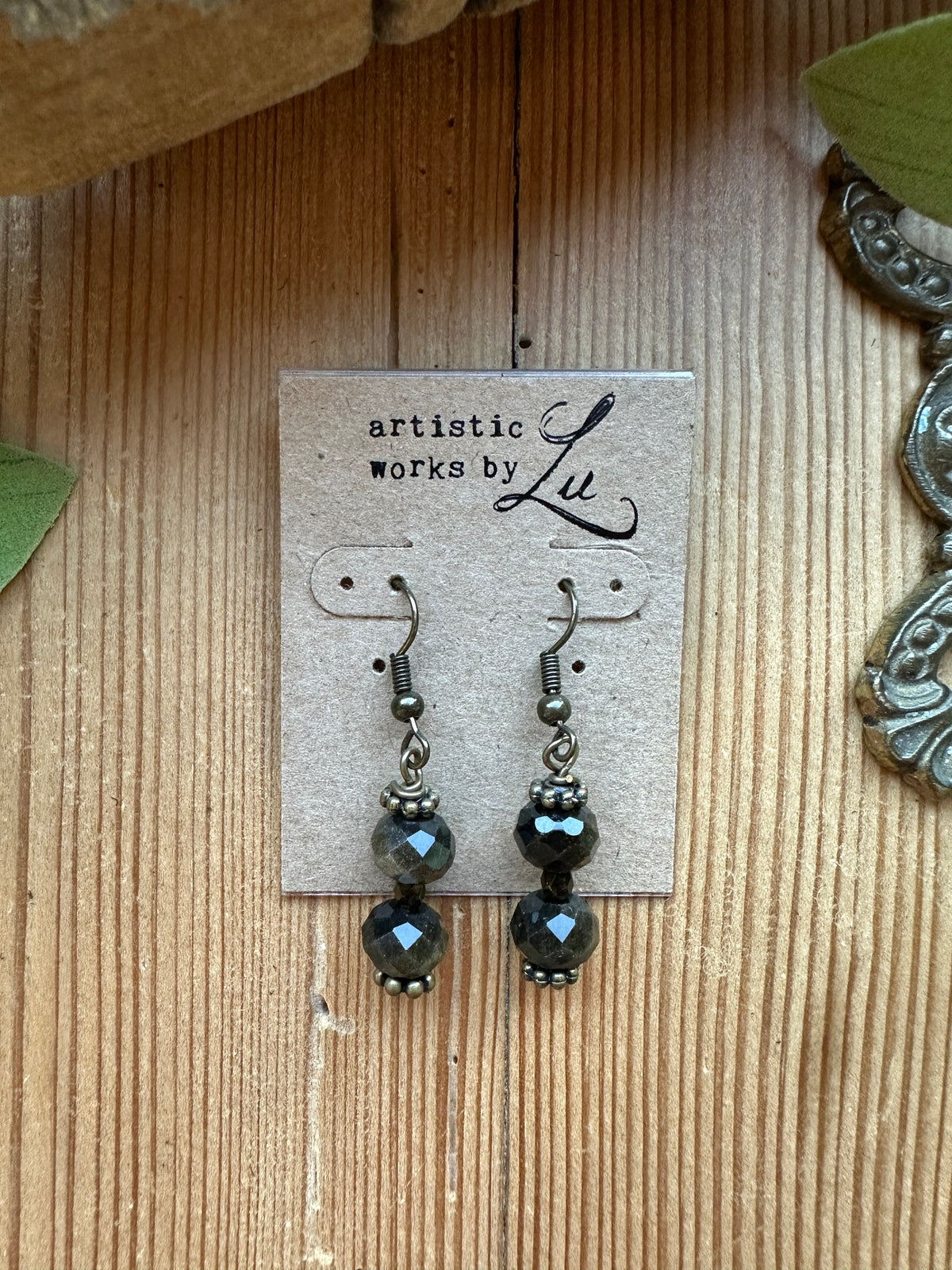 Sacred Ground Midnight Sheen Drop Earrings with faceted golden-sheen gemstone rondelles, pyrite beads, and antiqued brass ear wires on an Artistic Works By Lu card