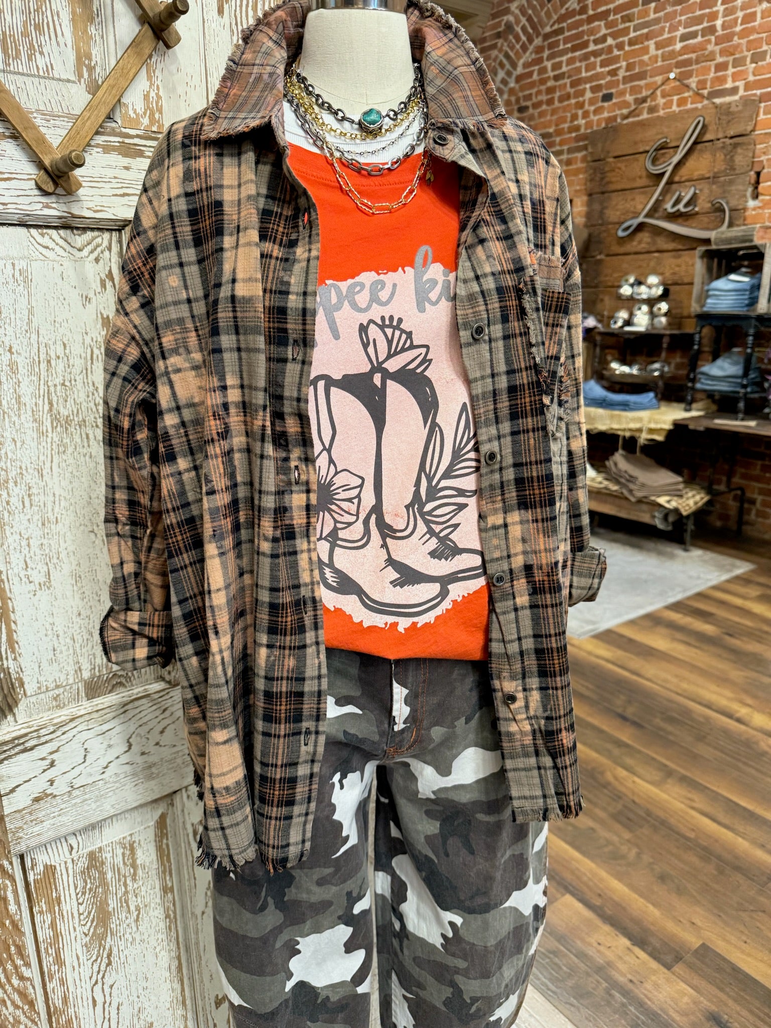 Mannequin wearing a plaid shirt, orange graphic t-shirt, and camouflage pants in a Leavenworth, KS boutique