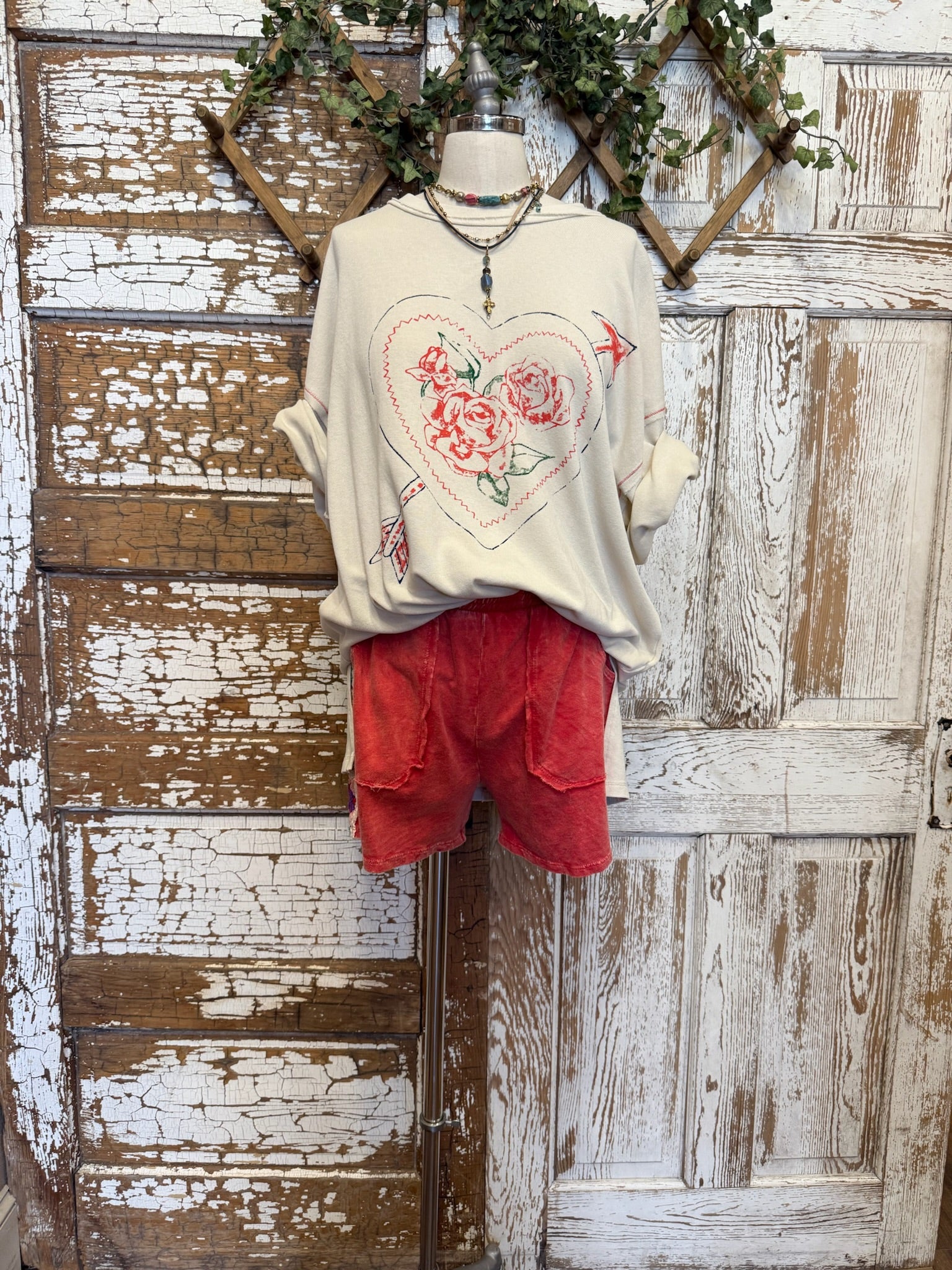 Mannequin wearing a cream graphic tee with floral heart design and red shorts against in Springfield, MO boutique