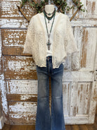 Mannequin wearing a beige lace top, cross pendant, turquoise layered jewelry and blue jeans against a rustic wooden background