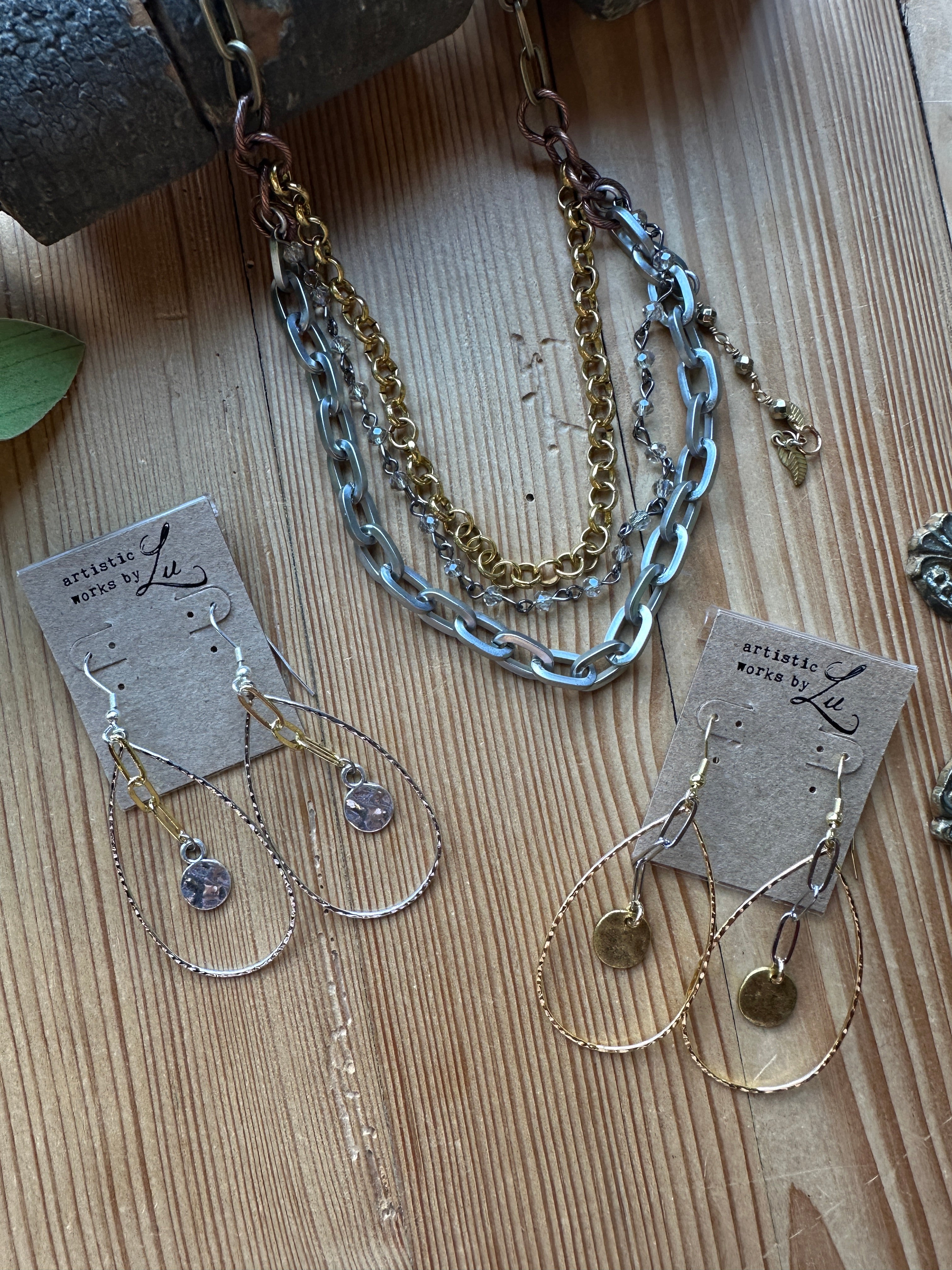Gold and antique silver chains with delicate beads in necklace and earrings with tags on a wooden surface