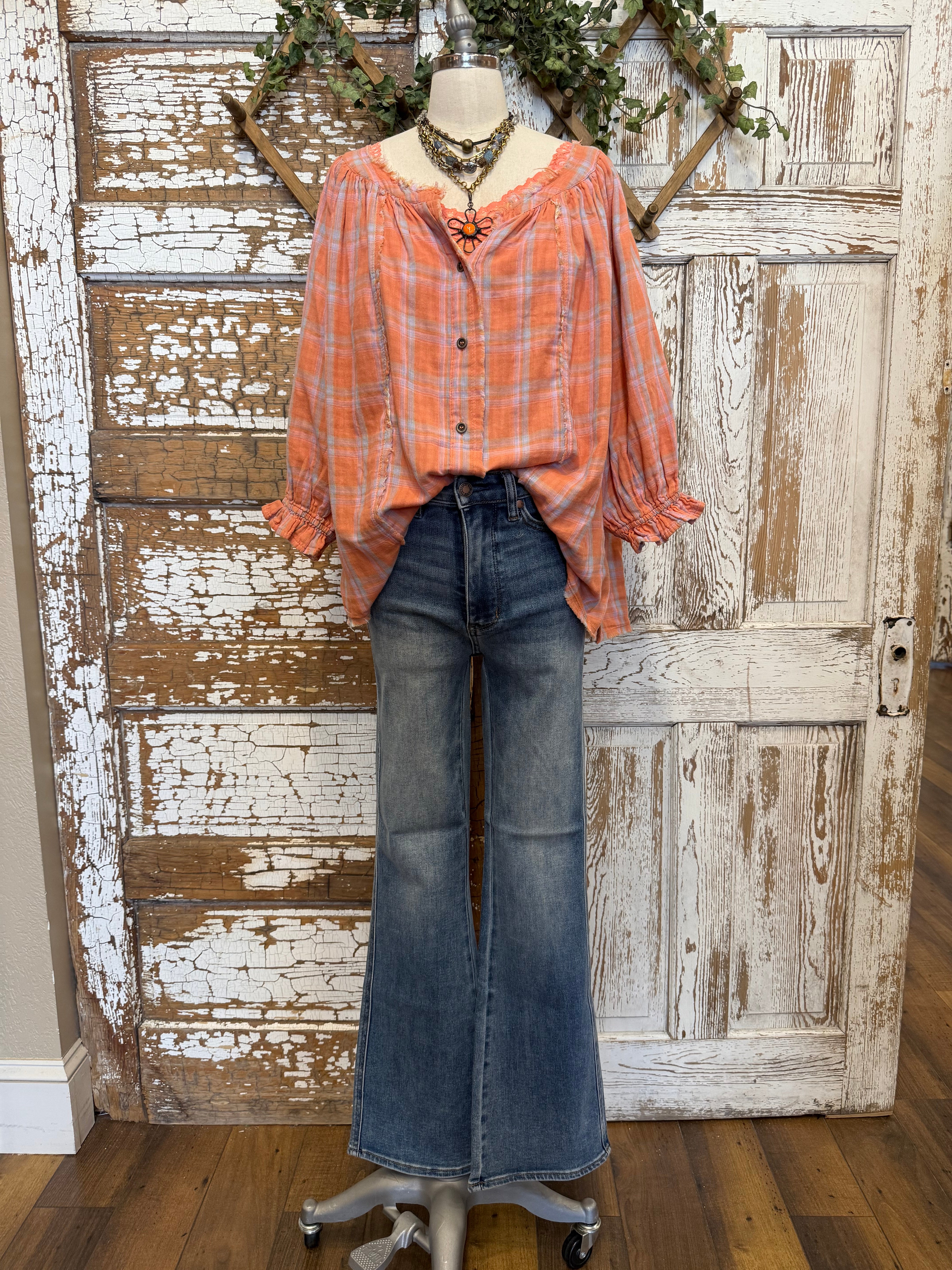 Mannequin wearing an orange and pink plaid shirt, handmade flower necklace and blue jeans against a rustic wooden wall in Leavenworth, KS boutique
