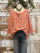 Mannequin wearing an orange and pink plaid shirt, handmade flower necklace and blue jeans against a rustic wooden wall in Leavenworth, KS boutique