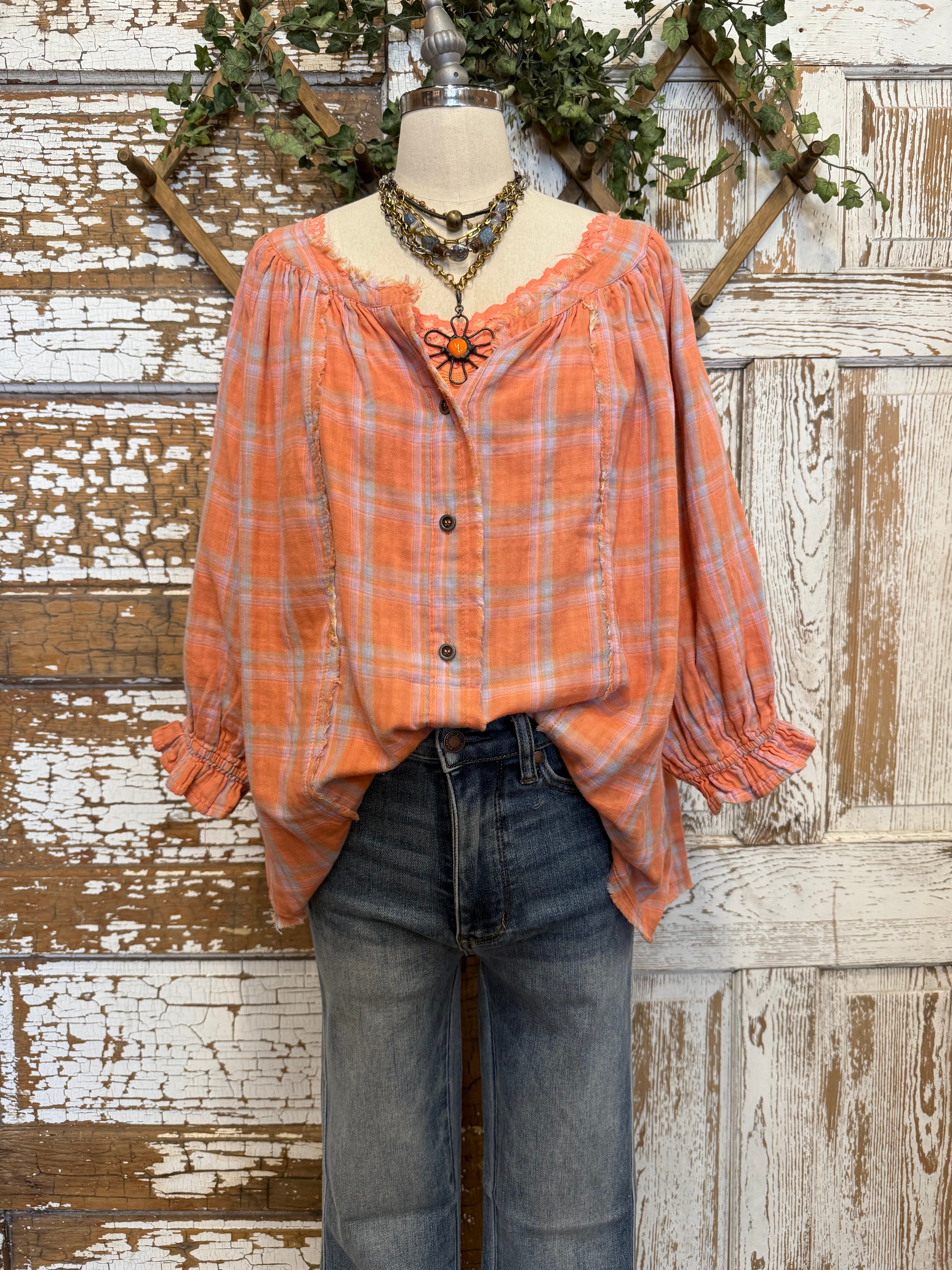 Mannequin wearing an orange and pink plaid shirt, handmade flower necklace and blue jeans against a rustic wooden wall in Leavenworth, KS boutique