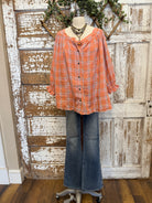 Mannequin wearing an orange and pink plaid shirt, handmade flower necklace and blue jeans against a rustic wooden wall in Leavenworth, KS boutique