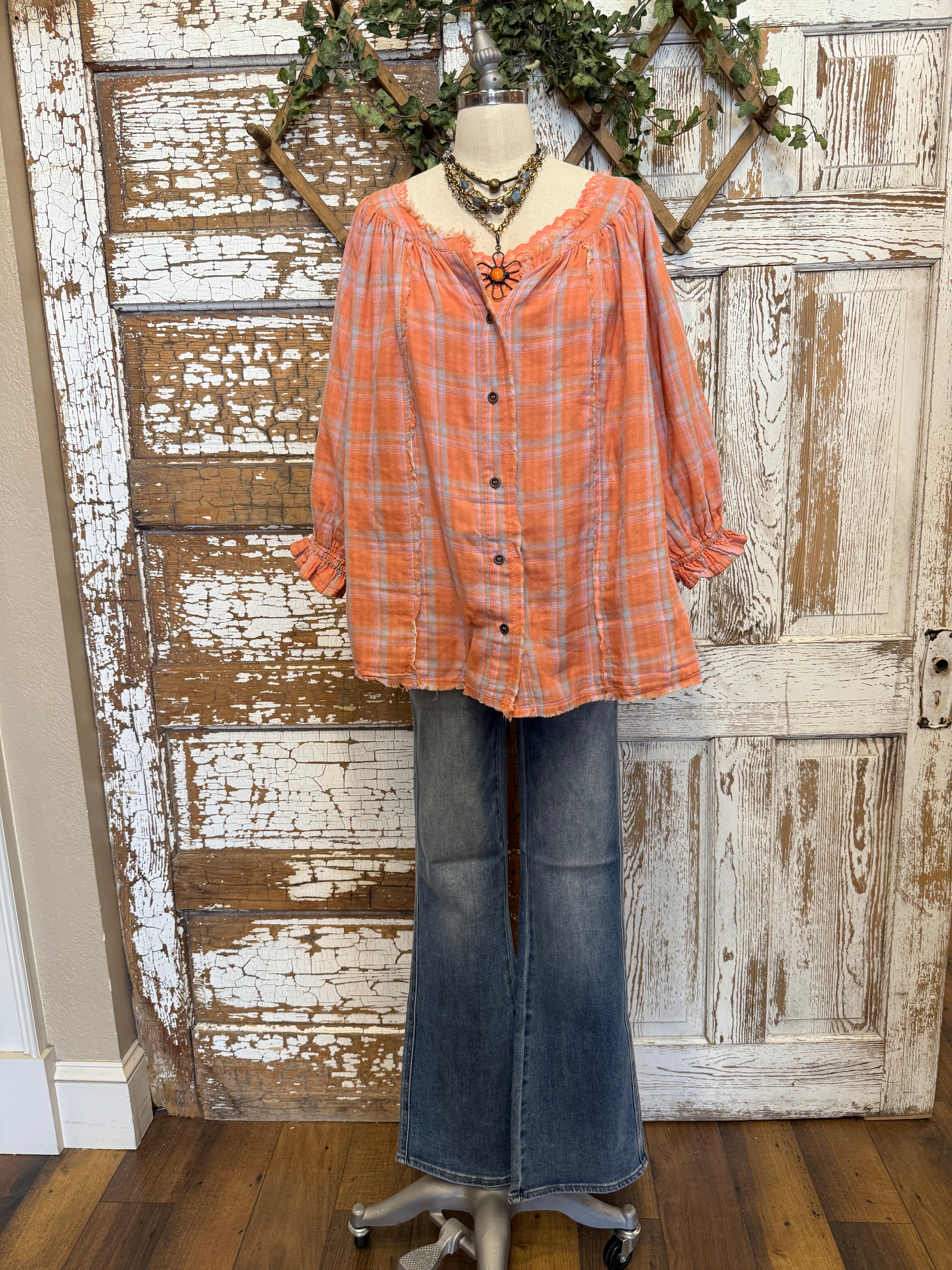 Mannequin wearing an orange and pink plaid shirt, handmade flower necklace and blue jeans against a rustic wooden wall in Leavenworth, KS boutique