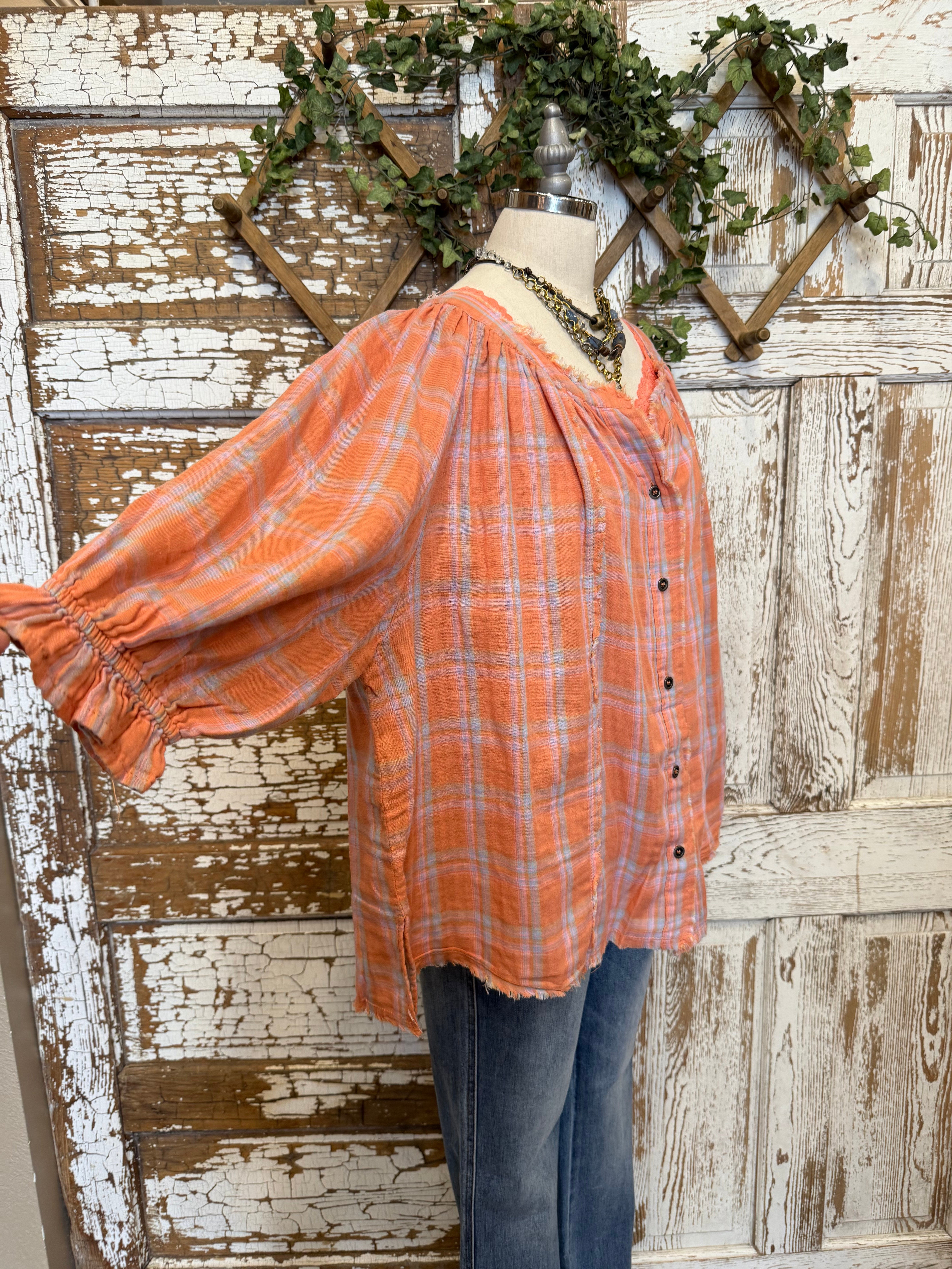 Mannequin wearing an orange and pink plaid shirt, handmade flower necklace and blue jeans against a rustic wooden wall in Leavenworth, KS boutique