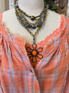 Mannequin wearing an orange and pink plaid shirt, handmade flower necklace and blue jeans against a rustic wooden wall in Leavenworth, KS boutique