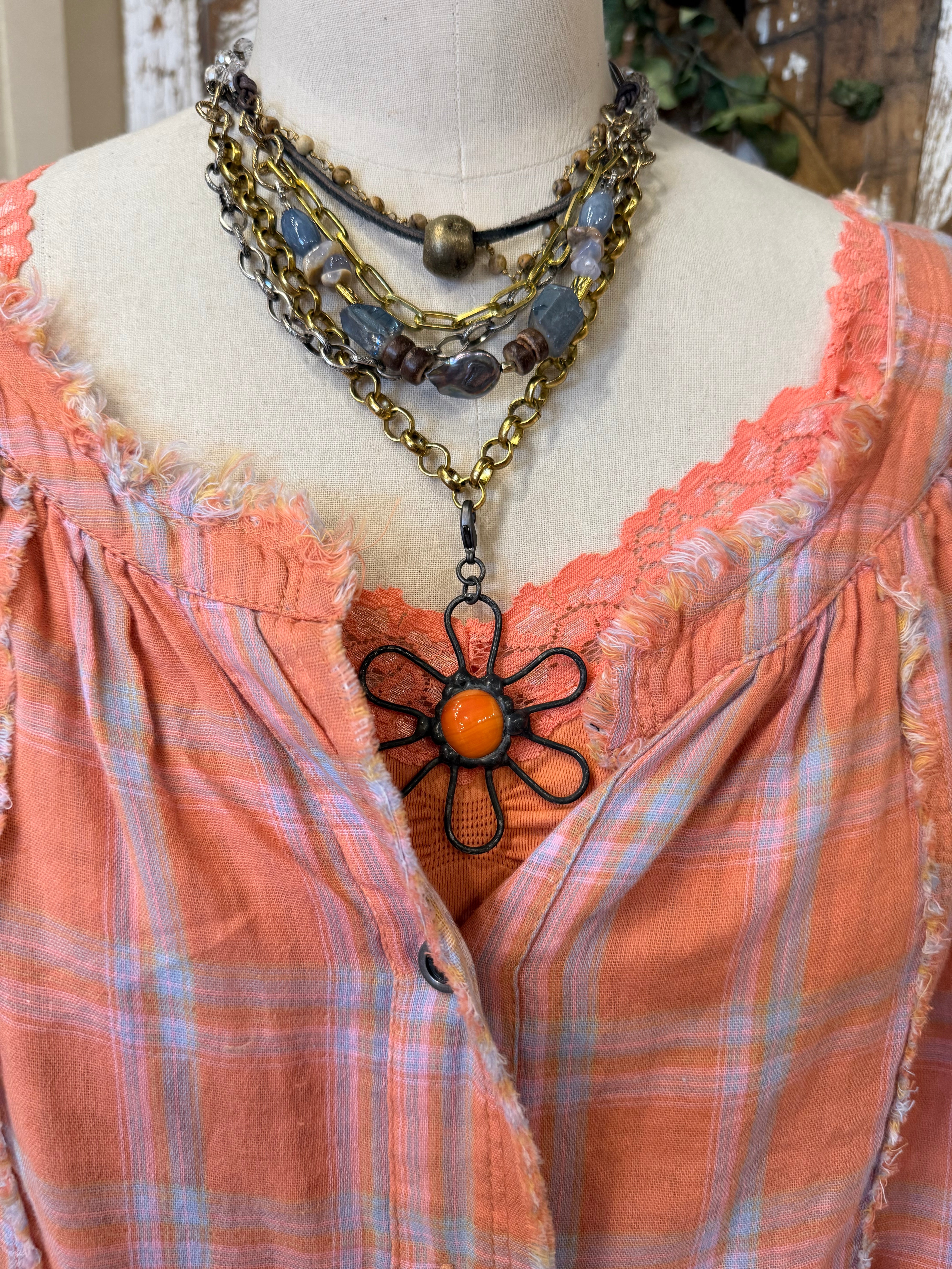 Mannequin wearing an orange and pink plaid shirt, handmade flower necklace and blue jeans against a rustic wooden wall in Leavenworth, KS boutique