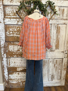 Mannequin wearing an orange and pink plaid shirt, handmade flower necklace and blue jeans against a rustic wooden wall in Leavenworth, KS boutique