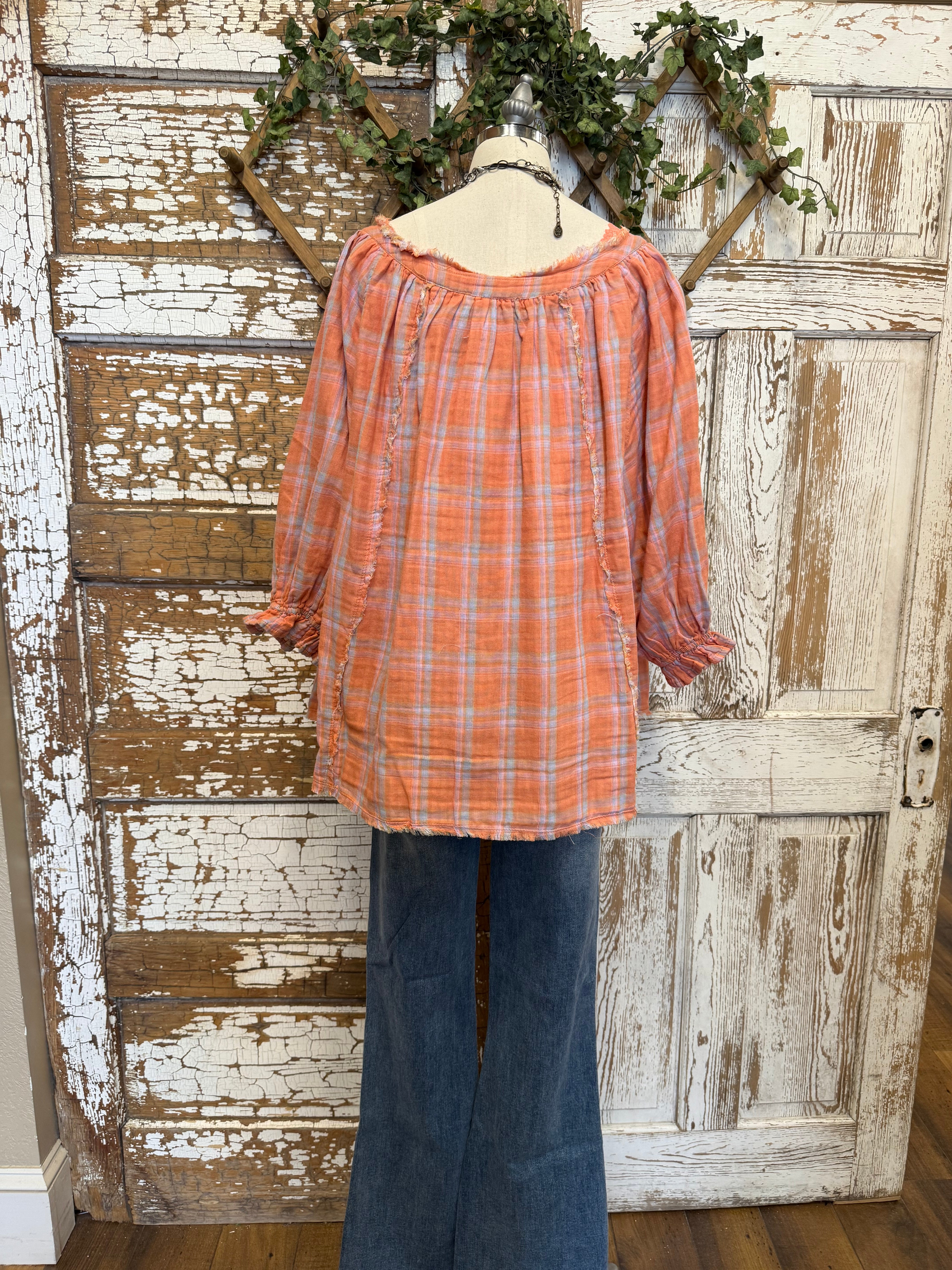 Mannequin wearing an orange and pink plaid shirt, handmade flower necklace and blue jeans against a rustic wooden wall in Leavenworth, KS boutique