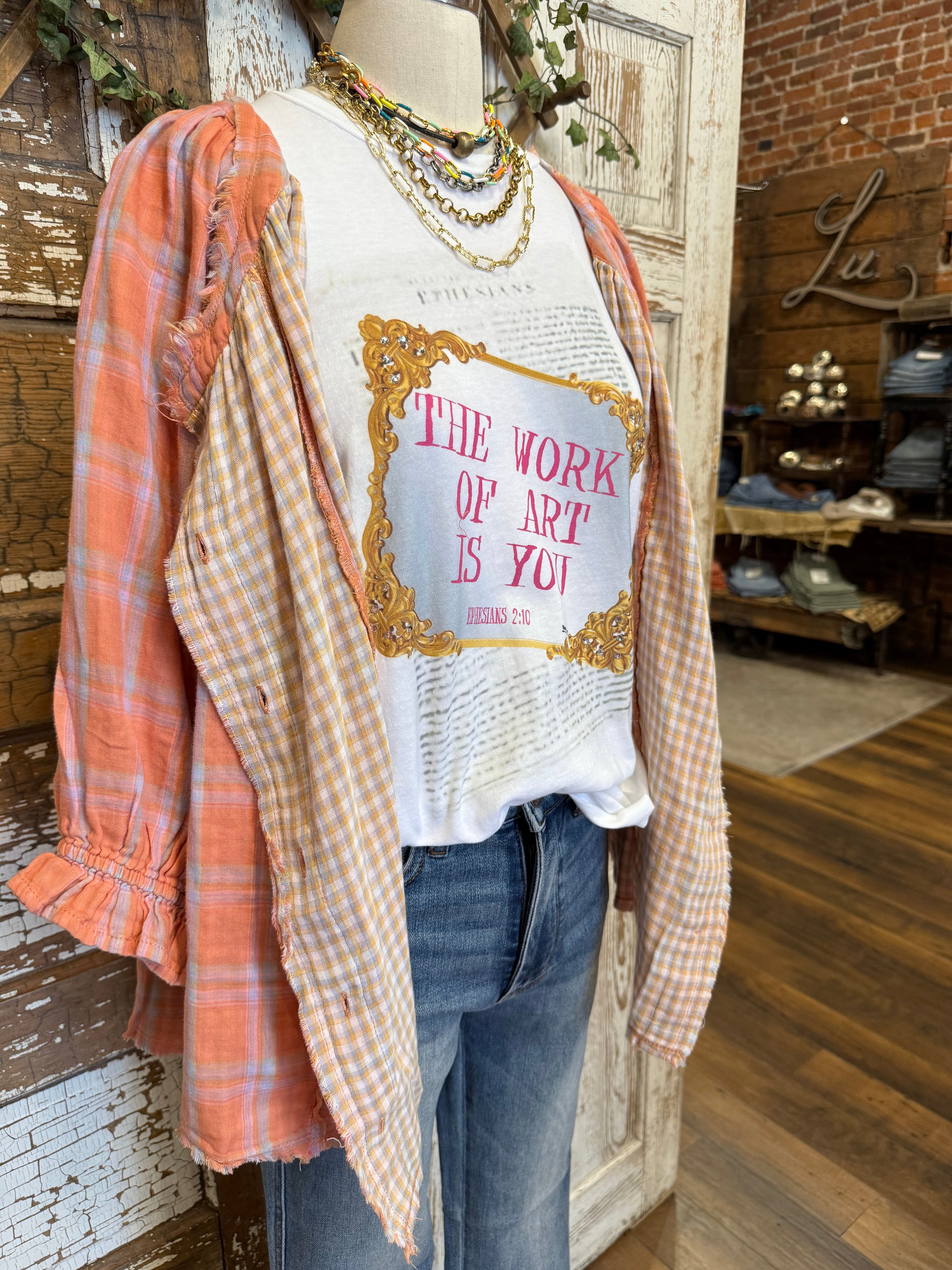 Mannequin wearing graphic tee and jeans with layered checkered button up shirt 
