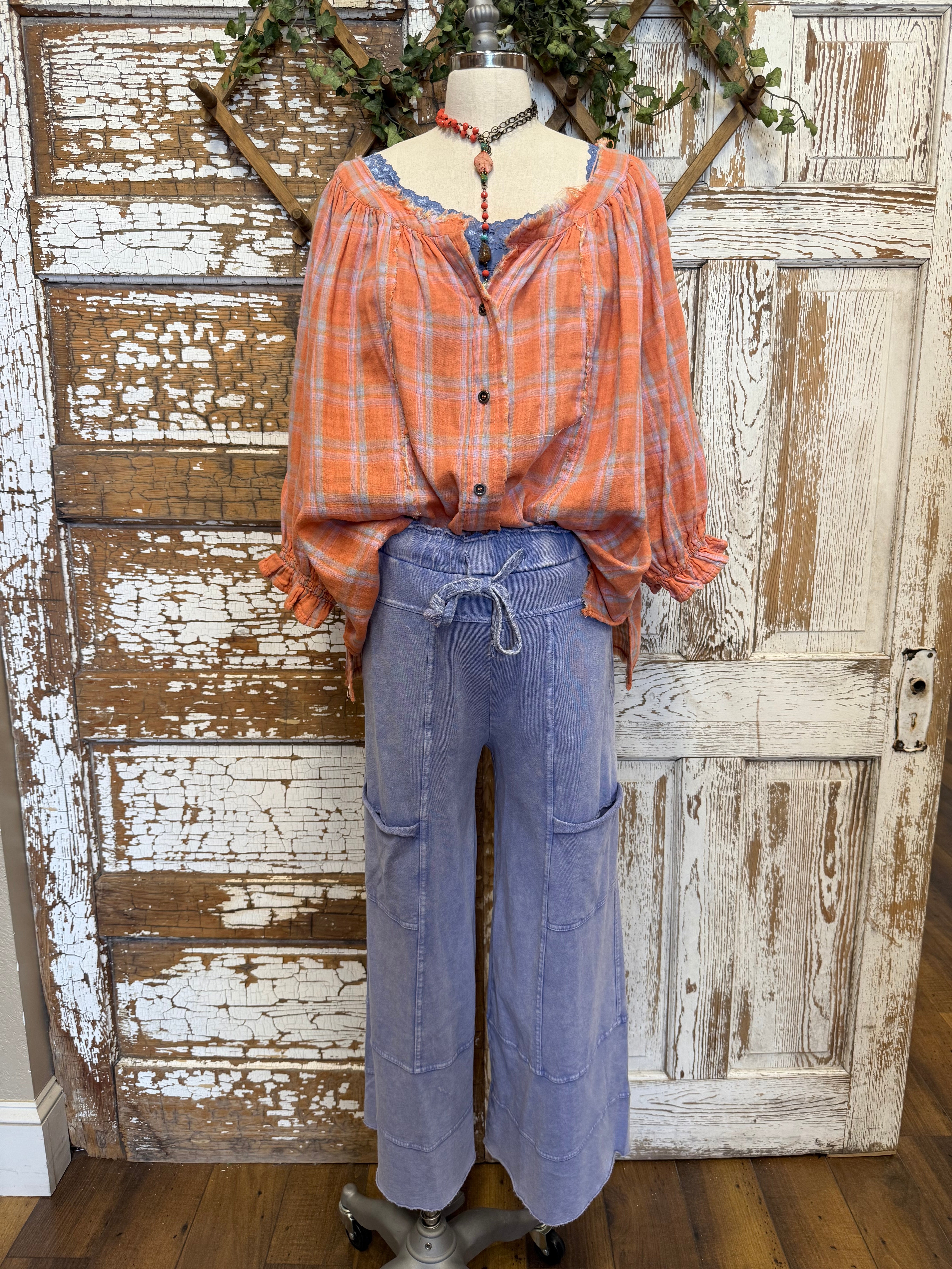 Mannequin wearing an orange and pink plaid shirt, handmade necklace and blue lounge wear against a rustic wooden wall in Leavenworth, KS boutique