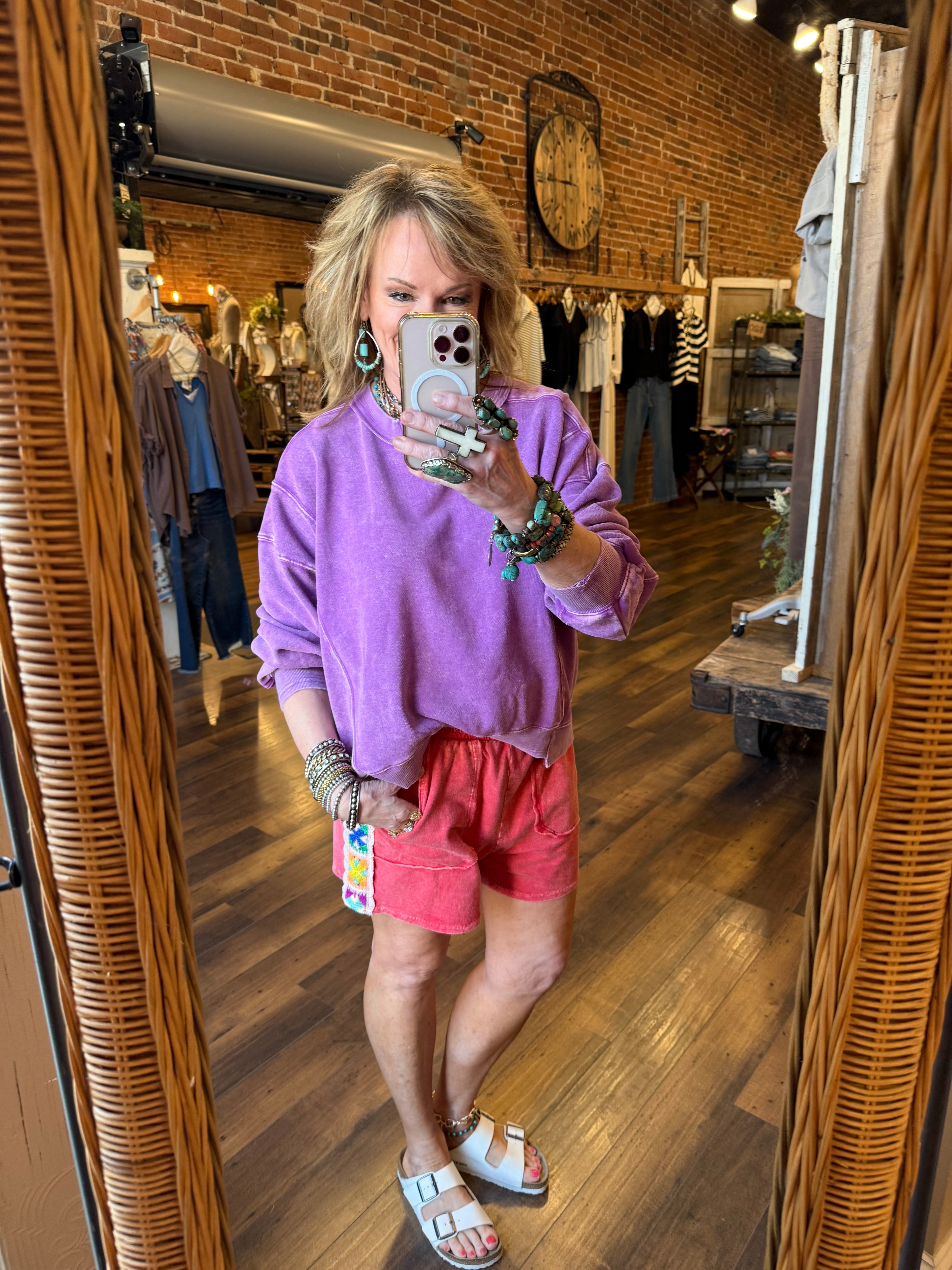 Lu taking a mirror selfie wearing a purple sweater and red shorts in Leavenworth, KS clothing boutique