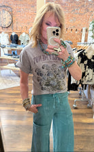 Lu taking a mirror selfie in a clothing store wearing a floral graphic t-shirt and teal leisurewear pants.