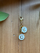 Gold-tone clip-on charm with white enamel K and C initial charms, paperclip link, and lobster clasp