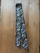 Olive paisley print silky twilly scarf laid flat on a wood surface