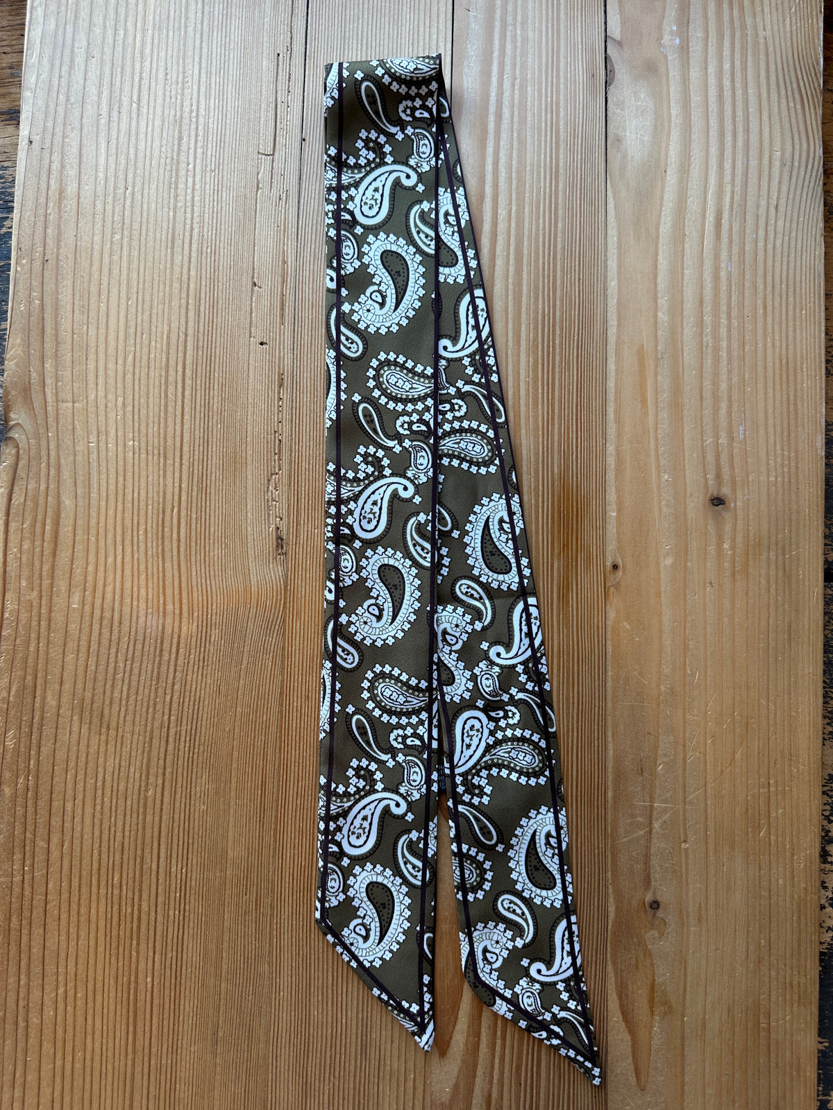 Olive paisley print silky twilly scarf laid flat on a wood surface
