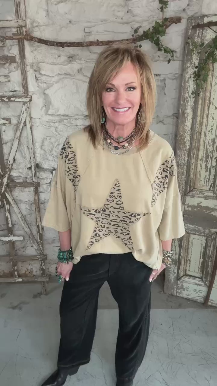 Lu wearing a star studded leopard top with leopard print accents and barrel jeans in boutique leavenworth, ks with handmade jewelry 