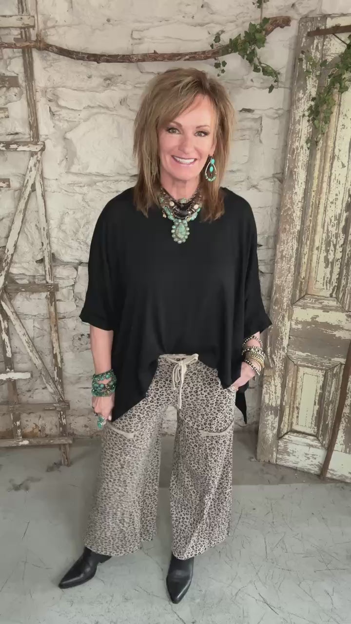 Lu wearing black flowy top and patterned leopard print pants against a rustic boutique springfield, mo