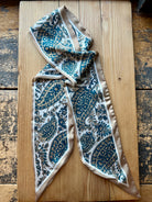 Teal paisley print silky twilly scarf laid flat on a wood surface
