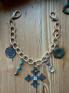Gold vintage charm chain with coin, cross, and flower charms laid flat on a wood surface