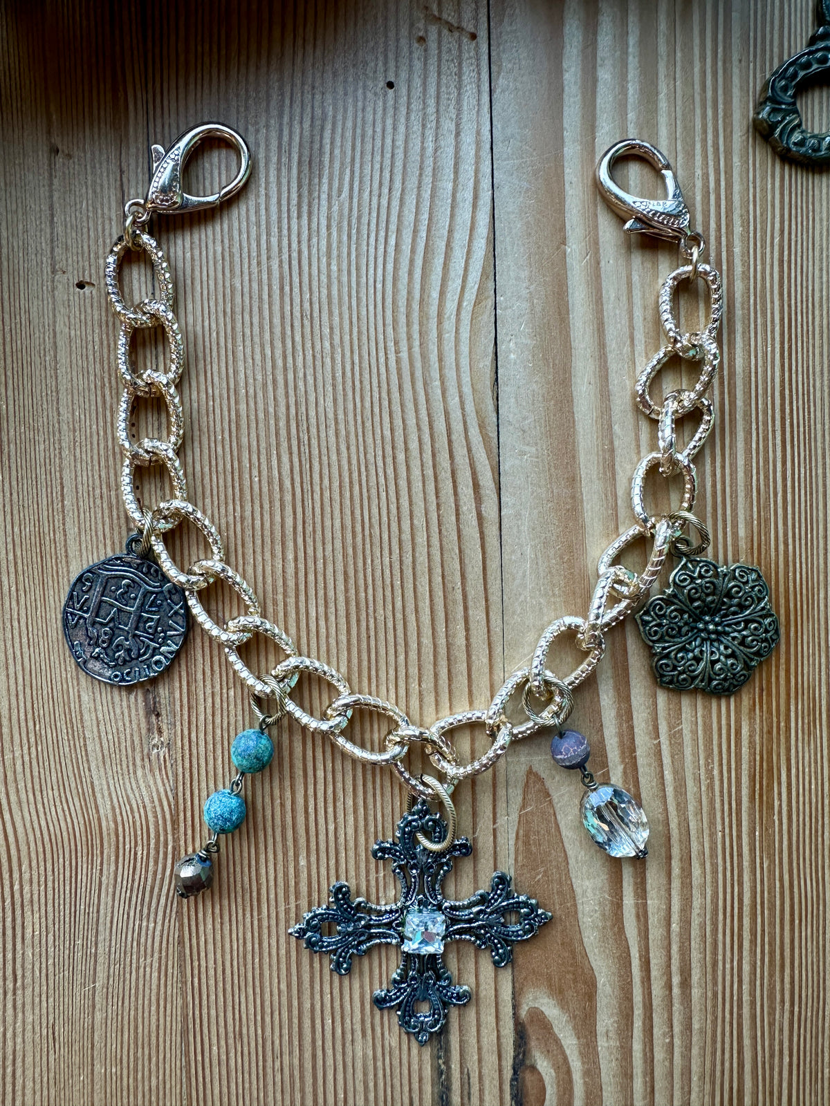 Gold vintage charm chain with coin, cross, and flower charms laid flat on a wood surface